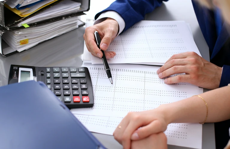 Dwie osoby analizujące dokument finansowy z&nbsp;kalkulatorem